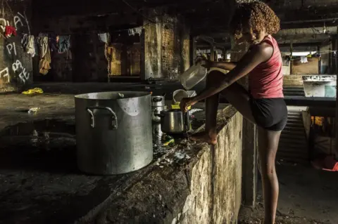 Tariq Zaidi Girl washing the dishes in the main stairway of the occupied IBGE building, 'Favela' Mangueira community, Rio de Janeiro, Brazil.