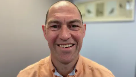 Kieran is smiling and wearing an orange shirt