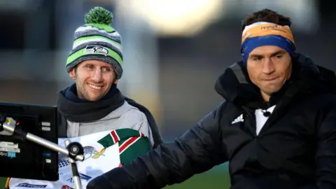 George Wood/Getty Images Sinfield embraces his friend Burrow at the end of a fundraising challenge. Sinfield wears his fundraising head band and a black thermal jacket, Burrow is wrapped in a woolly hat, scarf and blanket and smiles. Burrow's computer, which aided his speech, can be seen in the shot.