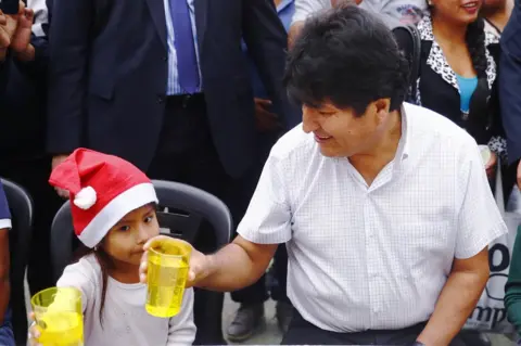 Getty Images Exiled former president of Bolivia Evo Morales talks to a girl during a Christmas breakfast with members of the Bolivian community of Buenos Aires at Campo De Deportes del Colegio Nacional de Buenos Aires on 25 December 2019 in Buenos Aires, Argentina