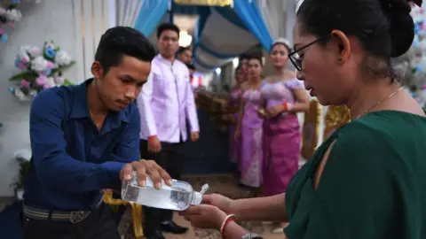 Getty Images A man shares hand sanitiser with a woman at a wedding service in Cambodia