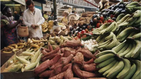 Getty Images Customers weigh up the bananas, sweet potatoes or yams and peppers on sale on a fruit and vegetable market stall, Brixton, London, England circa 1969. (Photo by RDImages/Epics/Getty Images)