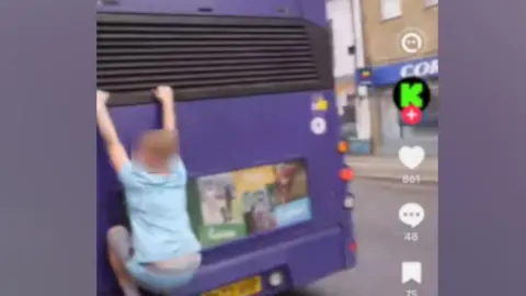 TikTok/J2Hundred A child hangs off the back of a moving bus in Norwich, seen in a grainy screenshot from a TikTok video