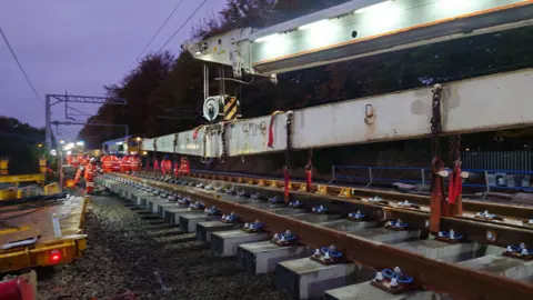 SRSA Colas Construction workers wearing orange hi-vis are working on a railway track at night.