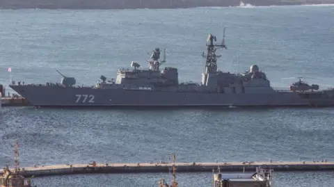 The Russian Neustrashimy frigate - a long, grey vessel with the number 772 printed on the side in white - in the water. 