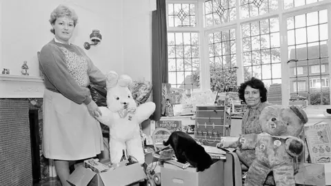 Alain Nogues/Getty Images A black and white image of Christmas 1984. Women in Rotherham stand with presents such as teddys and football table for families of striking miners.