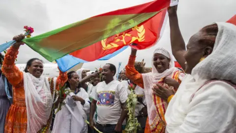 AFP Eritrean women hold up the flag of Eritrea on July 18, 2018, to welcome passengers of the flight from Ethiopian capital Addis Ababa, upon their arrival at the Asmara International airport. - Ethiopia and Eritrea on July 18, 2018,