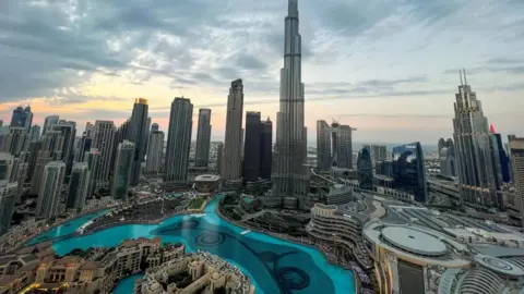 Reuters A presumption    of the Dubai skyline backing onto a brightening entity  featuring respective  skyscrapers and a man-made canal afloat  of glistening bluish  water