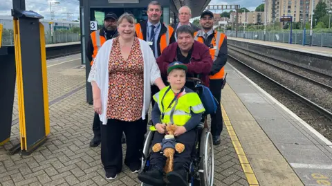 Luke Jeffrey/BBC Alfie and his family and railway staff on a platform