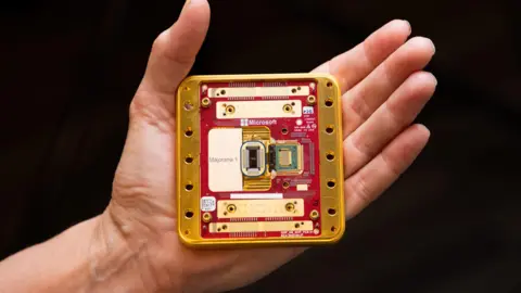 A photograph of the new Majorana 1 chip which is a gold and red square, held in the palm of an open hand (Microsoft press image)