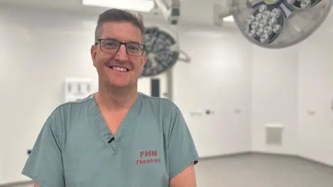 Consultant Craig White, dressed in blue scrubs, stands in a new operating theatre. 