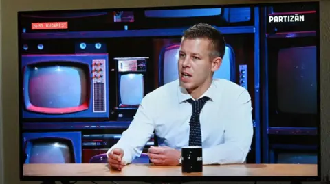 ATTILA KISBENEDEK/AFP A man in a white shirt speaks in front of a set showing old TVs