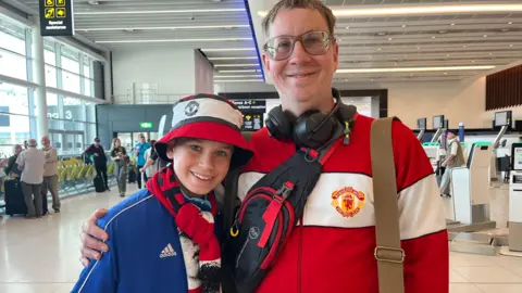 Davina Ramos/BBC Sam Warburton has a Manchester United scarf and bush hat while his dad Andy has glasses greying brown hair and is wearing a Manchester United tracksuit top.