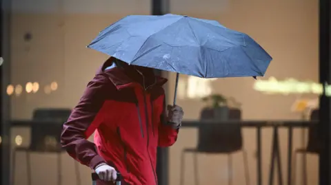 A person under an umbrella wearing a raincoat in heavy rain