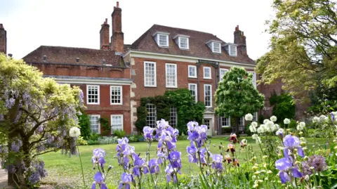 The National Trust A stately home surrounded by grass and flowers and trees