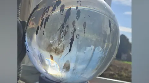 Northamptonshire Fire and Rescue Service A large glass sphere, sitting on a living room windowsill. There are burn marks on the glass and some reflections. An item is next to the ornament. A window is behind. 