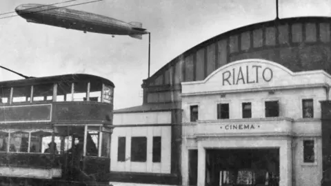 The R38 Airship seen above the Rialto Cinema in Hull, in June 1921. There is also a tram in the photograph.