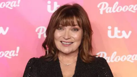 Getty Images Lorraine Kelly in front of a pink branded background covered in logos