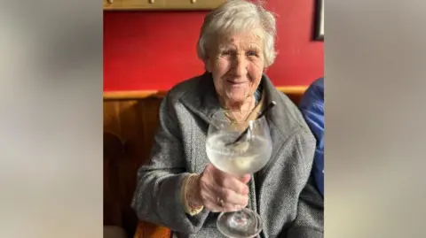 Supplied Image of Hilda in a grey coat holding up a gin and tonic