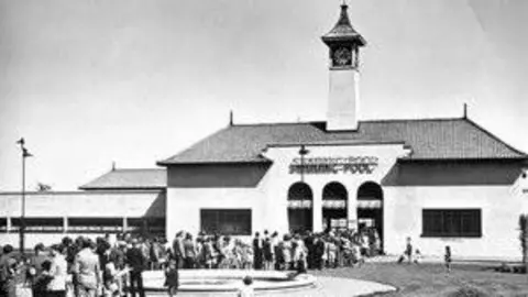 Friends of Peterborough Lido A black and white image of the Lido building with people queuing outside.