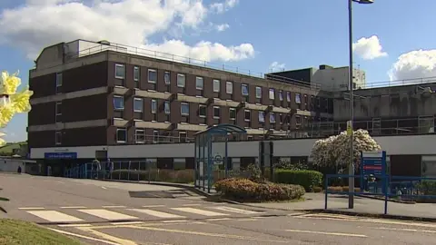 A view of the front of North Devon District Council. The building is brown and has four levels with many small windows. There is a sign to the right of the building and a zebra crossing at the centre.