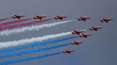 Reuters Ten red aircrafts, with red, white and blue smoke behind them, flying in a V formation from left to right.
