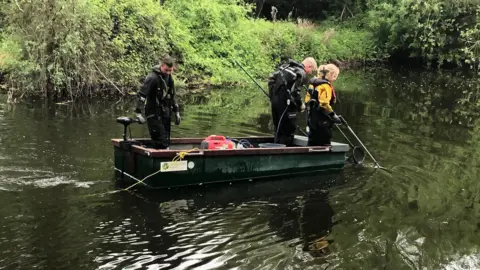 Environment Agency Three Environment Agency staff members are in a small boat on a lake. They are using nets to find fish