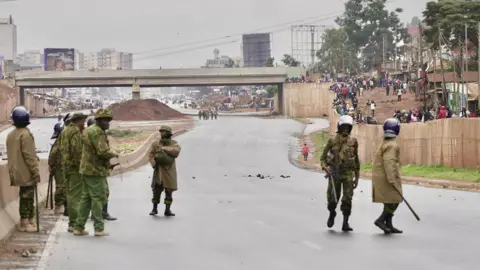 Police in uniform block a highway leading to Nairobi. Crowds of people are seen in the background