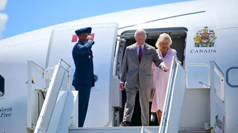 King Charles III and Queen Camilla walking off a plane