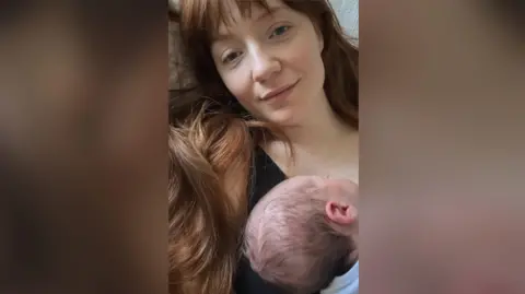 Nicola Roberts, who has long red hair with a fringe, is seen sitting down with her newborn baby on her chest