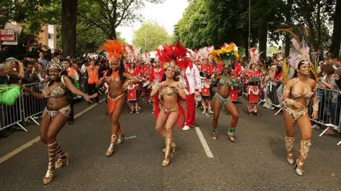 Getty Images A group of dancers in colourful outfits dance through a road in Luton at Luton Carnival