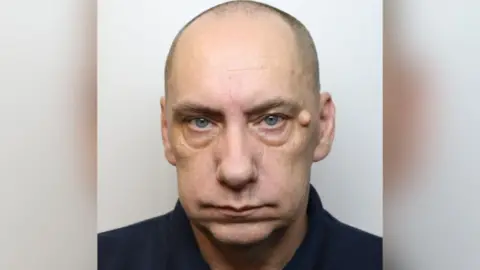 Wiltshire Police A custody shot of Mark Bellas. He is bald and has blue eyes. He is pictured against a white background, looking straight at the camera with a blank expression.
