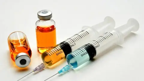 Syringes with blue and orange liquid. There are bottles of orange liquid beside the syringes.