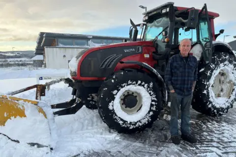 El conductor de tractor Duncan Wight de pie junto a su tractor cubierto de nieve.