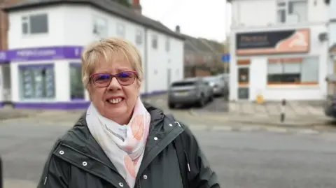 BBC A woman with a dark jacket and scarf stood in the street