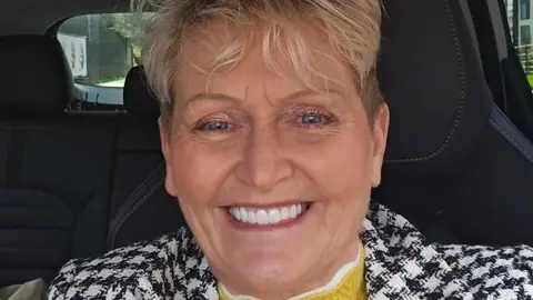 Jamiel Slaney-Summers Jamiel Slaney-Summers in a smiling selfie. She is wearing a black and white coat and a yellow and white jumper. She is sat in a car, which has black seats. She has short hair and is wearing make up. She has white, well kept teeth. 