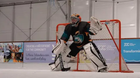 A player stands guard in the goals on an ice rink.