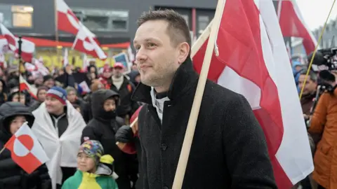 AFP via Getty Images Greenland's Head of Government (Naalakkersuisut) Jens-Frederik Nielsen, holds a Greenlandic flag as he attends a demonstration to the US consulate in Nuuk, Greenland on January 17, 2026. 