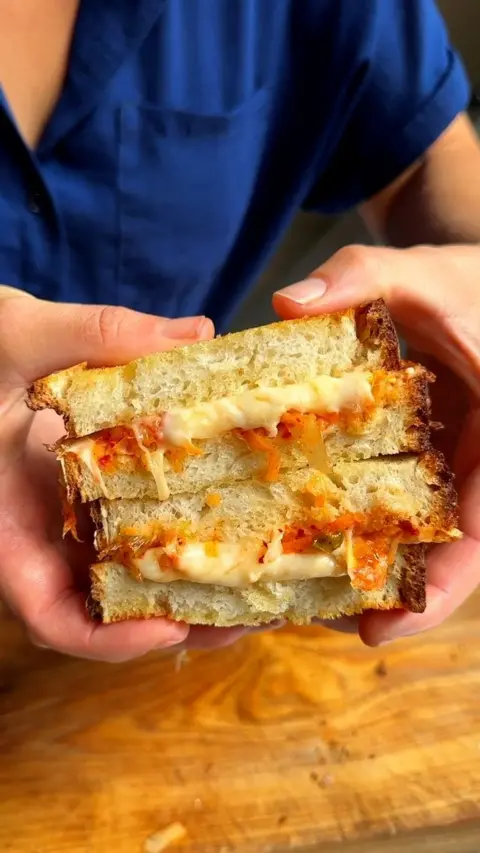 A woman waring a blue top holds a toasted sandwich with cheese 