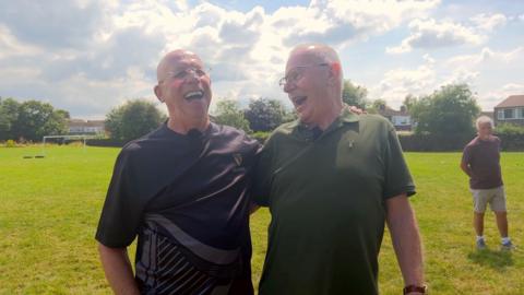 Image of two men. They have their arms around each other and are laughing