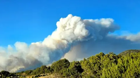 Jacob Lake Inn via CBS Newspath Picture of smoke rising over the mountains at Arizona fire with a blue sky in the background