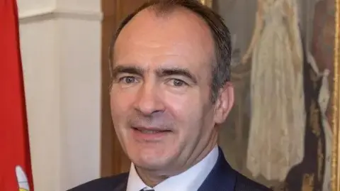 IOM GOVERNMENT Alfred Cannan, who has short dark hair with a receding hairline and is wearing white shirt and dark suit jacket.