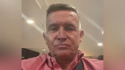 A man wearing a pink top, looking at the camera.