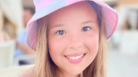 Imogen, who is 12, wears a pink sun hat and is smiling at the camera