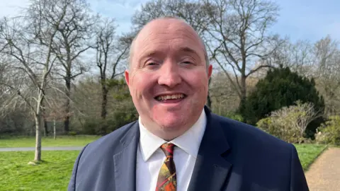 Lucinda Adam/BBC Michael Jones wears a suit in a park.