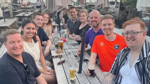Ten people sitting around a bench in a pub garden.