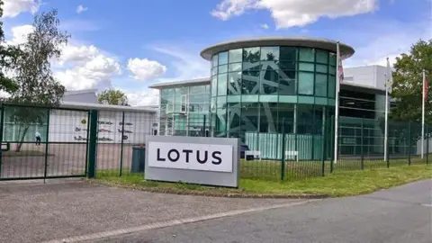 Sports car manufacturer Lotus to cut 550 jobs at Norfolk base 3 Martin Giles/BBC The outside of the Lotus building in Hethel, near Wymondham. The building is a curved glass building with a sign outside the front which says LOTUS in black letters.