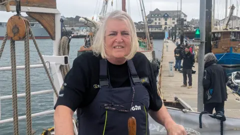 Rachel Dawson stood on the ship before it departed on the expedition. She is looking straight at the camera and is smiling. 