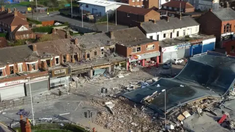 Image shows the completely destroyed precinct of shops in New Ferry, Wirral, after an explosion in 2017