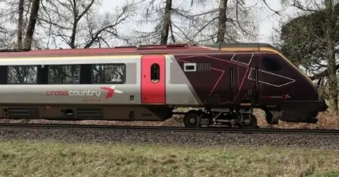 The cab and first carriage of a CrossCountry train is on the track in the countryside.